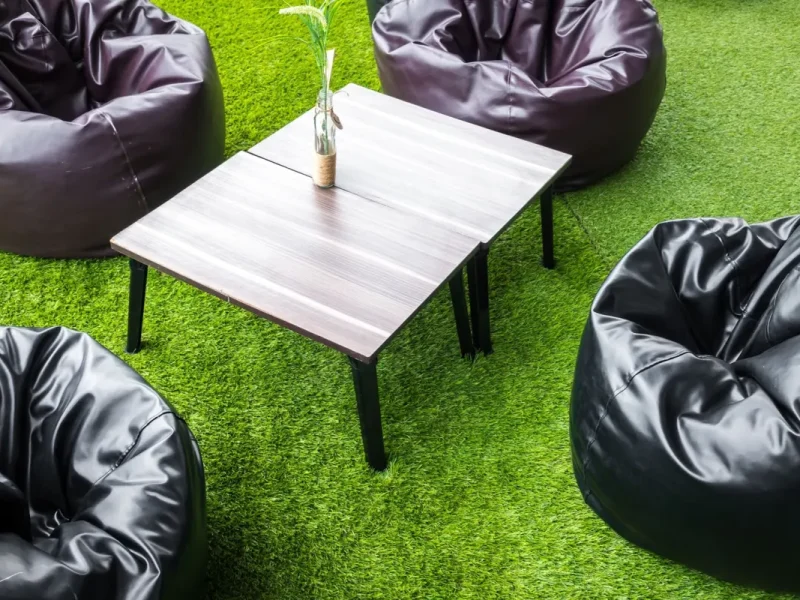 Terraza con césped artificial, mesa baja de madera y puffs negros