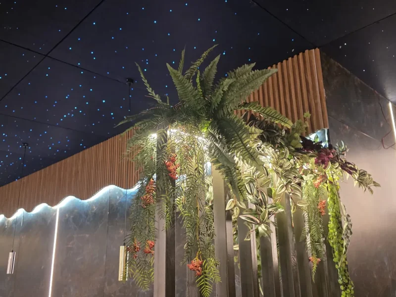 Jardinera artificial iluminada sobre separador de madera en un restaurante