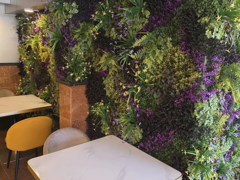 Jardín vertical artificial con flores moradas y amarillas junto a las mesas de un restaurante